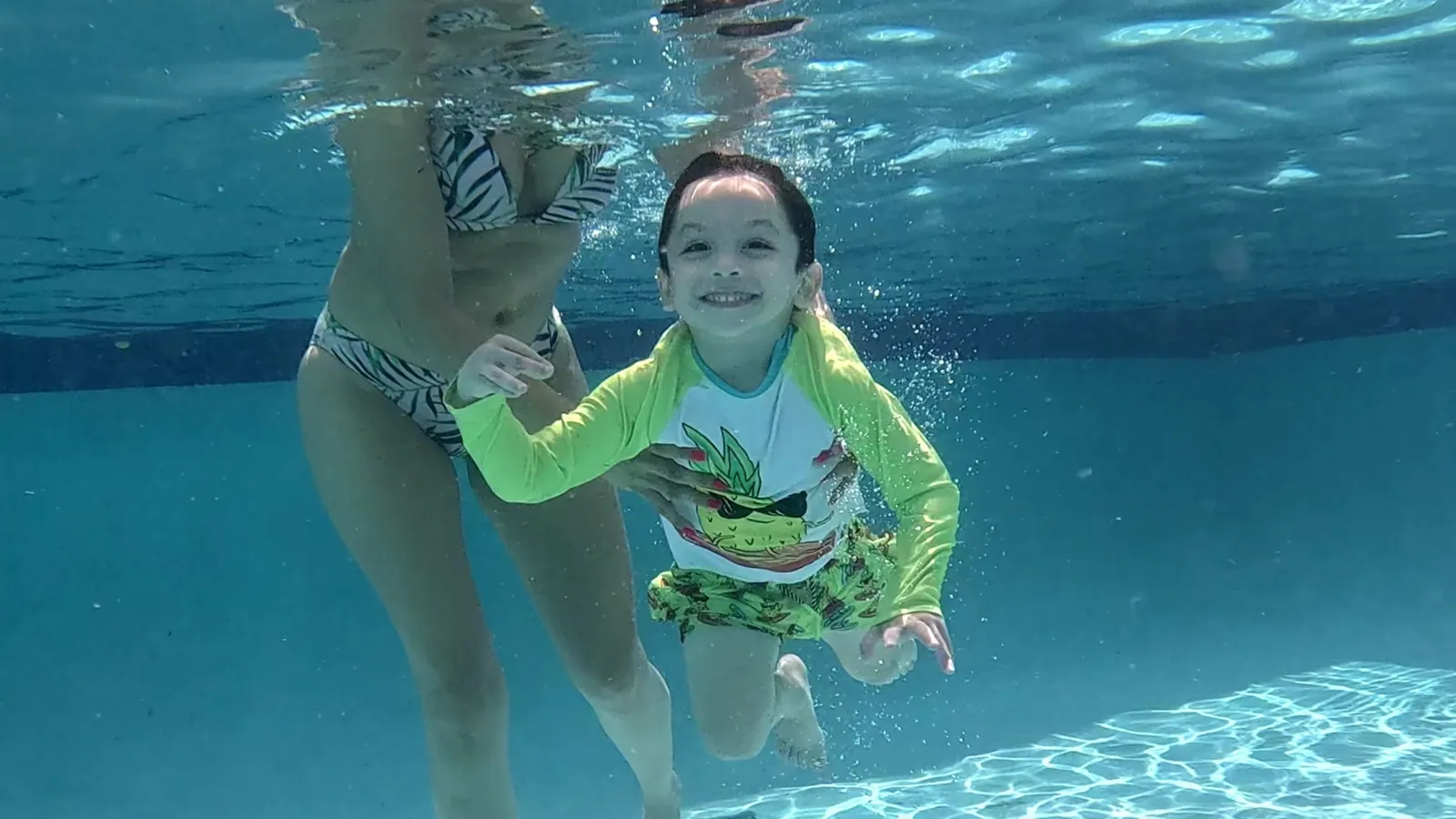 Niña sonriente nadando bajo el agua junto a su instructora