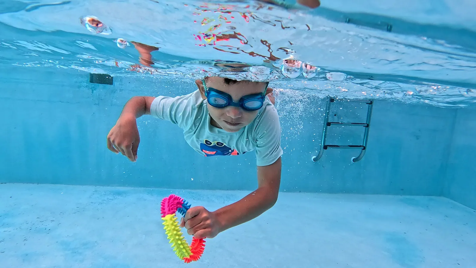 Niño con gafas sosteniendo un juguete de piscina bajo el agua