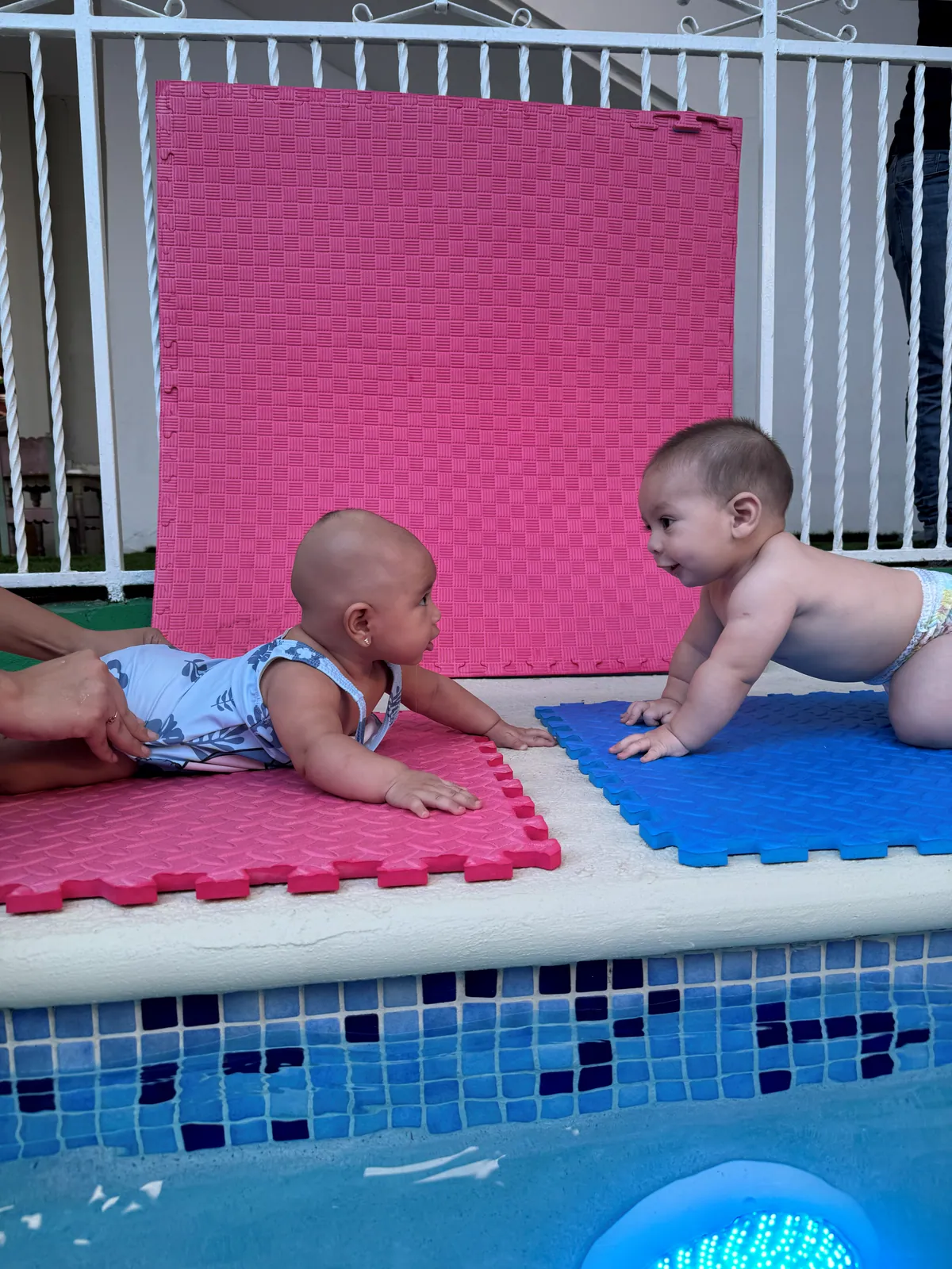 Dos bebés gateando sobre colchonetas junto a la piscina